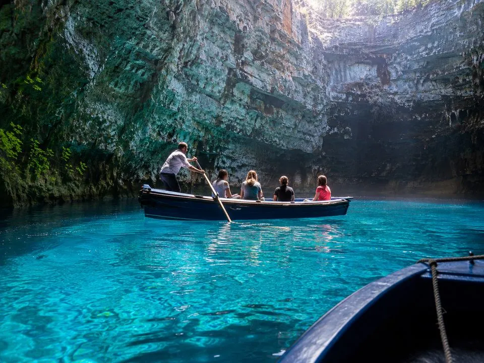 A shared rowing boat with a boatman crossing the open chamber of Melissani Cave